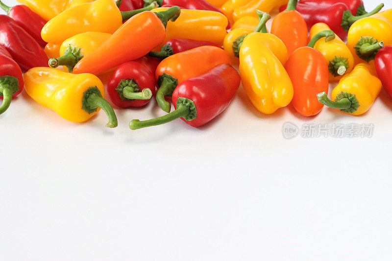 一堆红色、黄色和橙色的迷你辣椒(Capsicum annuum)的特写图片，白色背景上有绿色的茎，复制空间